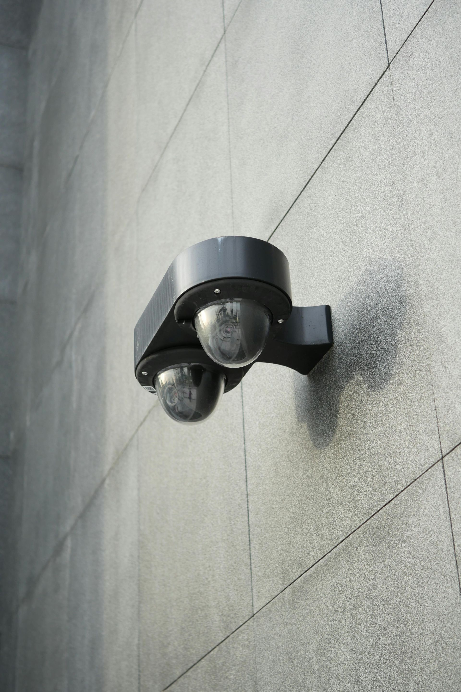 Two black security cameras mounted on a textured gray building wall.