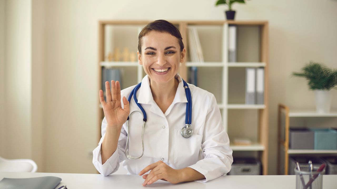 Smiling doctor in a white coat holding up a smartphone in a bright clinic office
