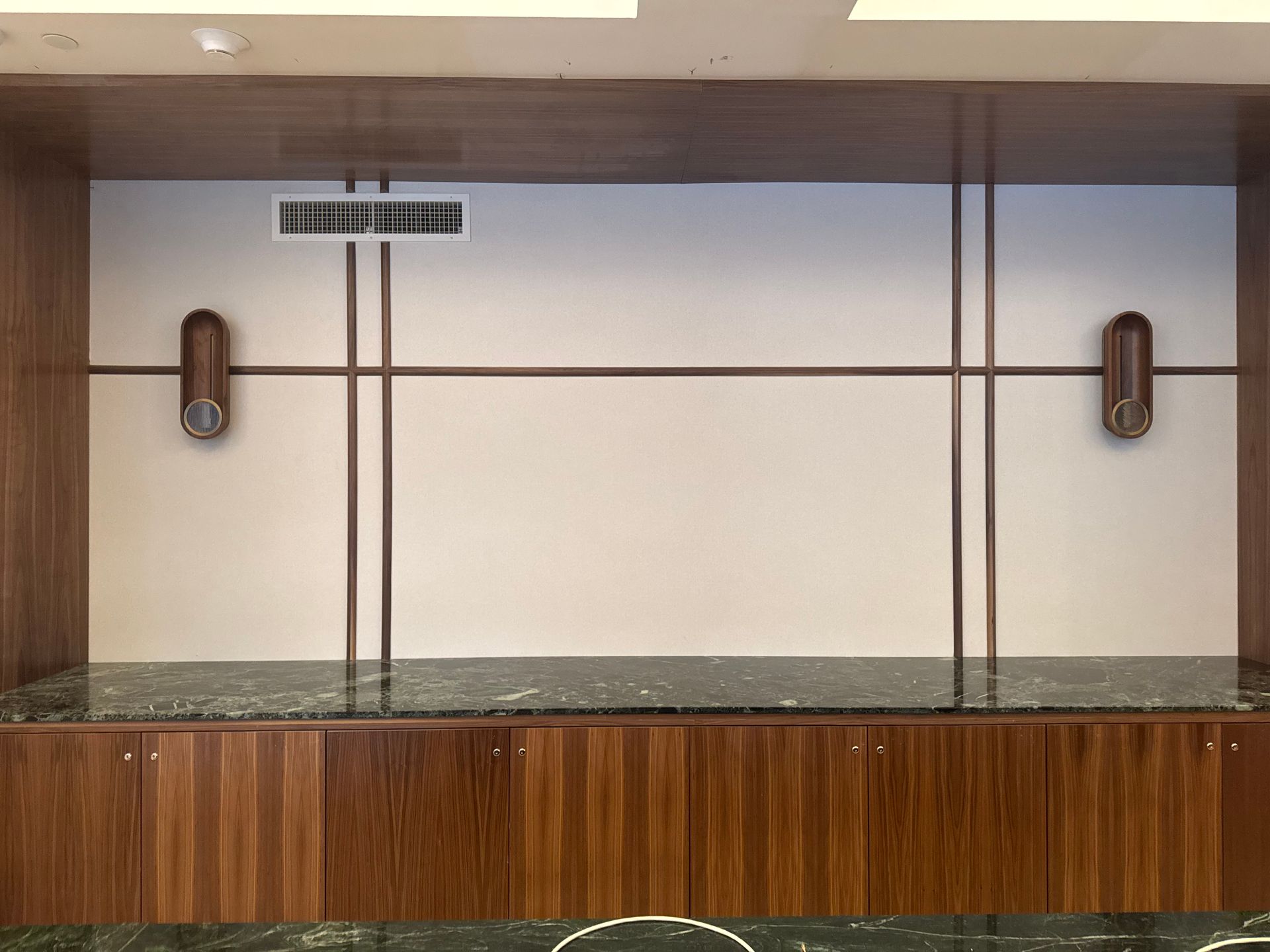 Wooden wall with built-in cabinetry, marble countertop, decorative metal lines, and sconce lighting.