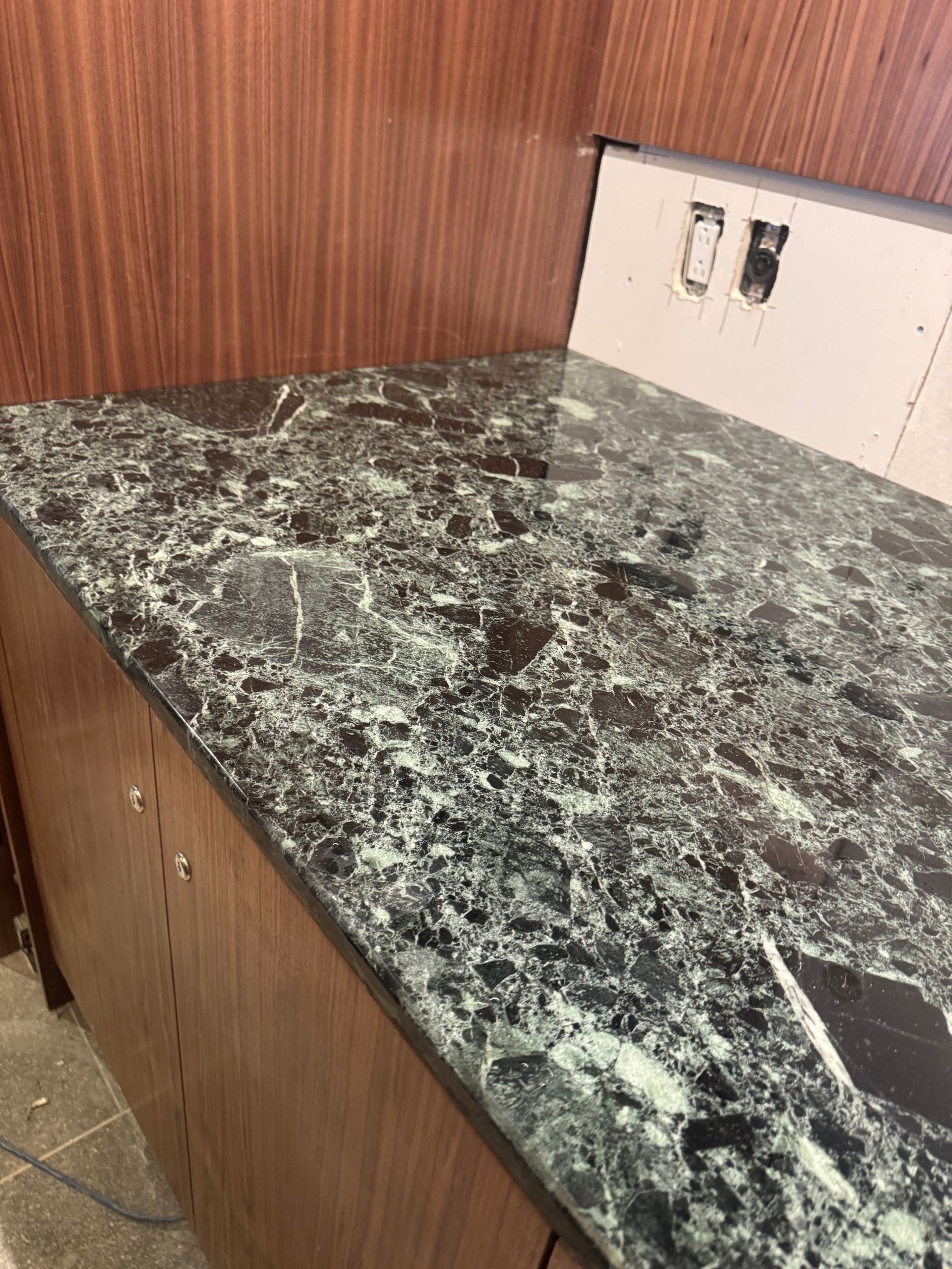Countertop with a marble-like pattern. Wooden cabinets below, wooden paneling on the wall behind, and electrical outlet cutout.