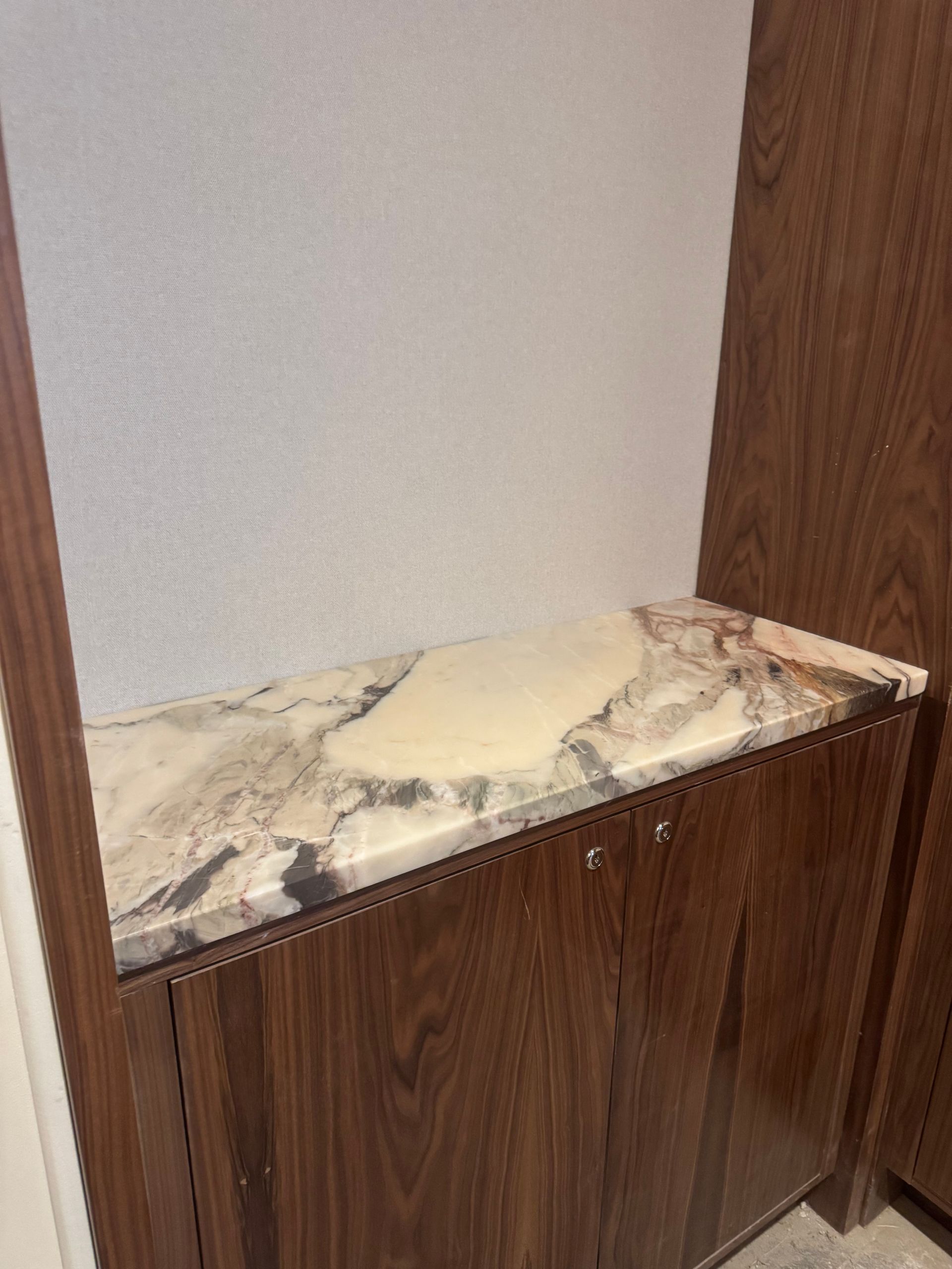 A built-in dark wood cabinet with a marble countertop against a white wall.