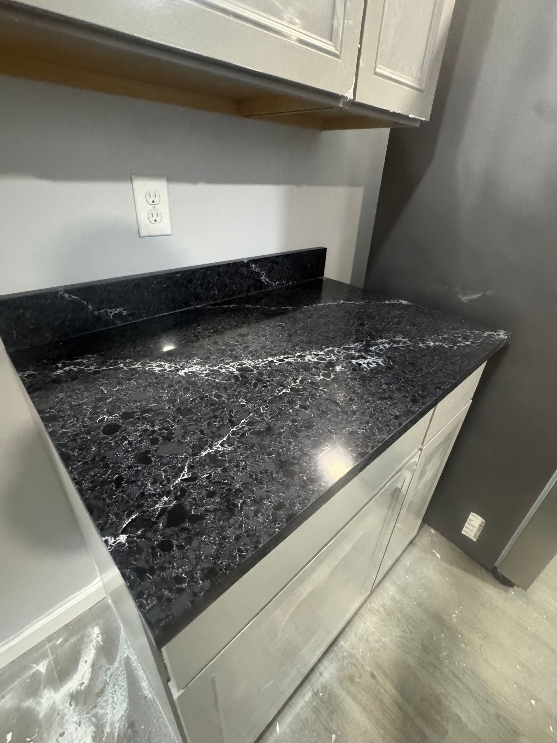 Black granite countertop installed in a kitchen with gray cabinets and a light gray wall.