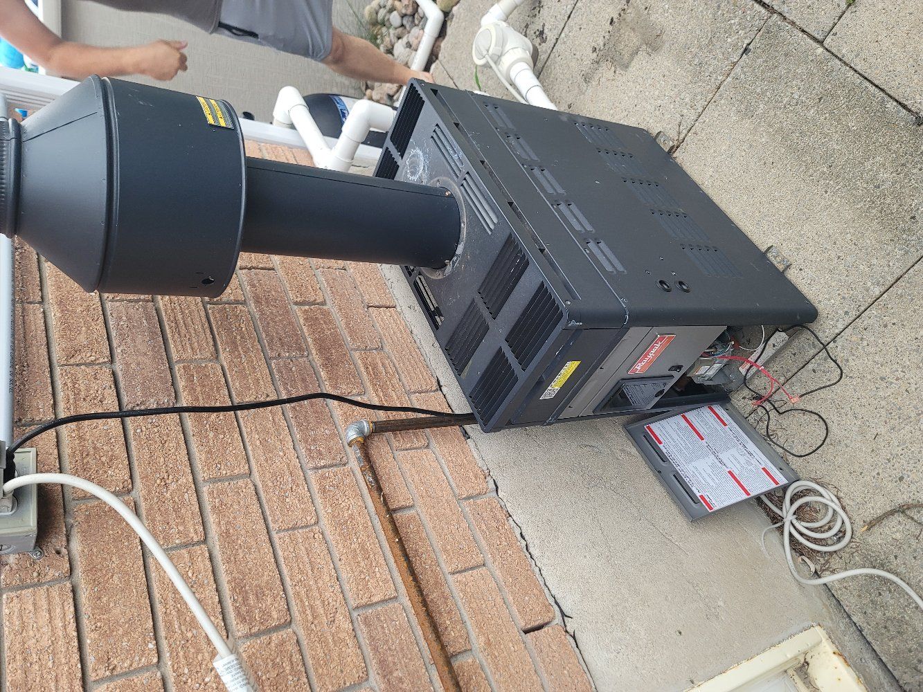 Black machine with long cylinder attached on a brick surface with a person working nearby.