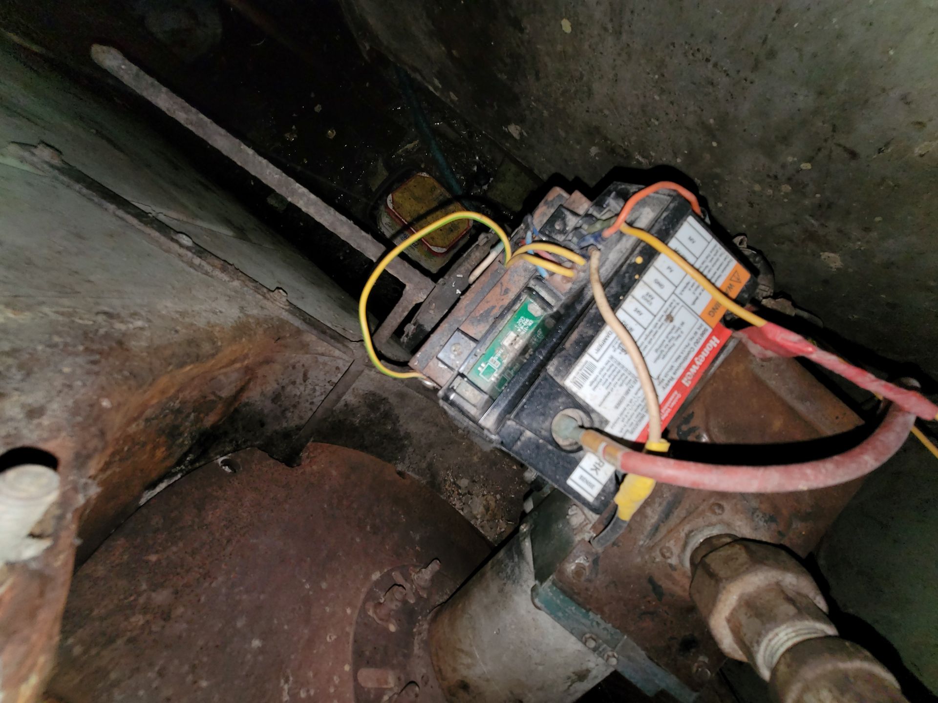 Electrical junction box with wires, mounted in a rusty, dark mechanical space.