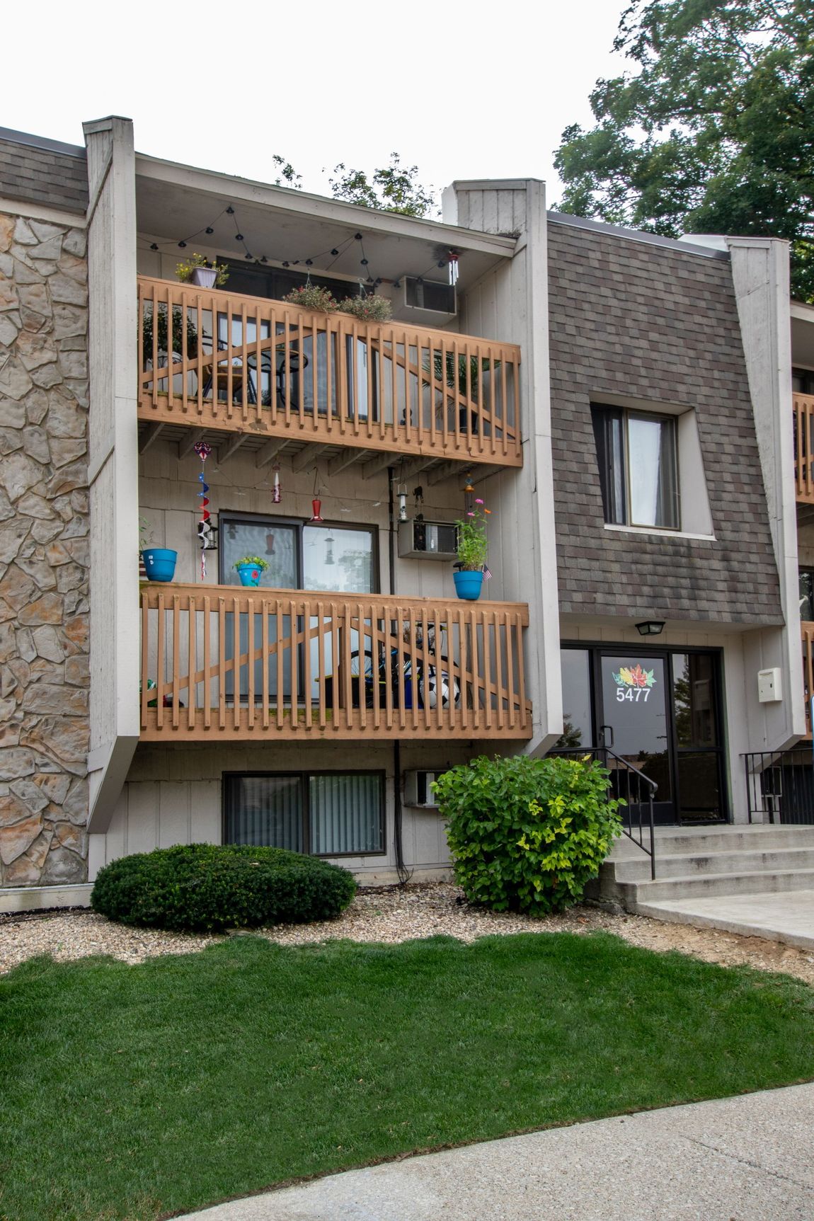 Apartment building with two wooden balconies, tan facade, and green lawn.