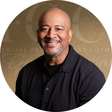 Smiling man with shaved head and salt and pepper beard wearing a black shirt, set against a brown background.