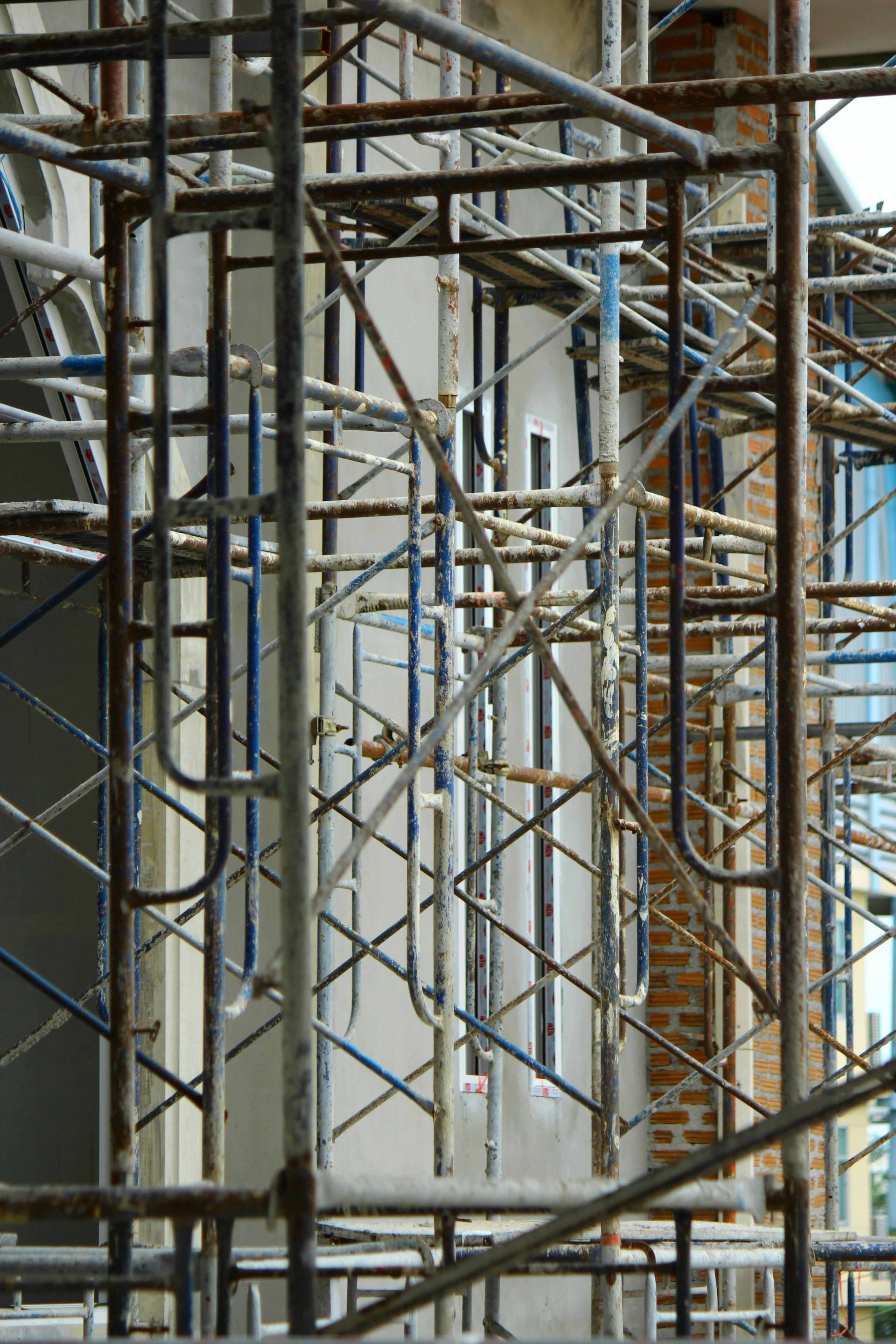 Échafaudage entourant la façade d'un bâtiment, composé de barres métalliques ; certaines peintes en bleu, visibles derrière.