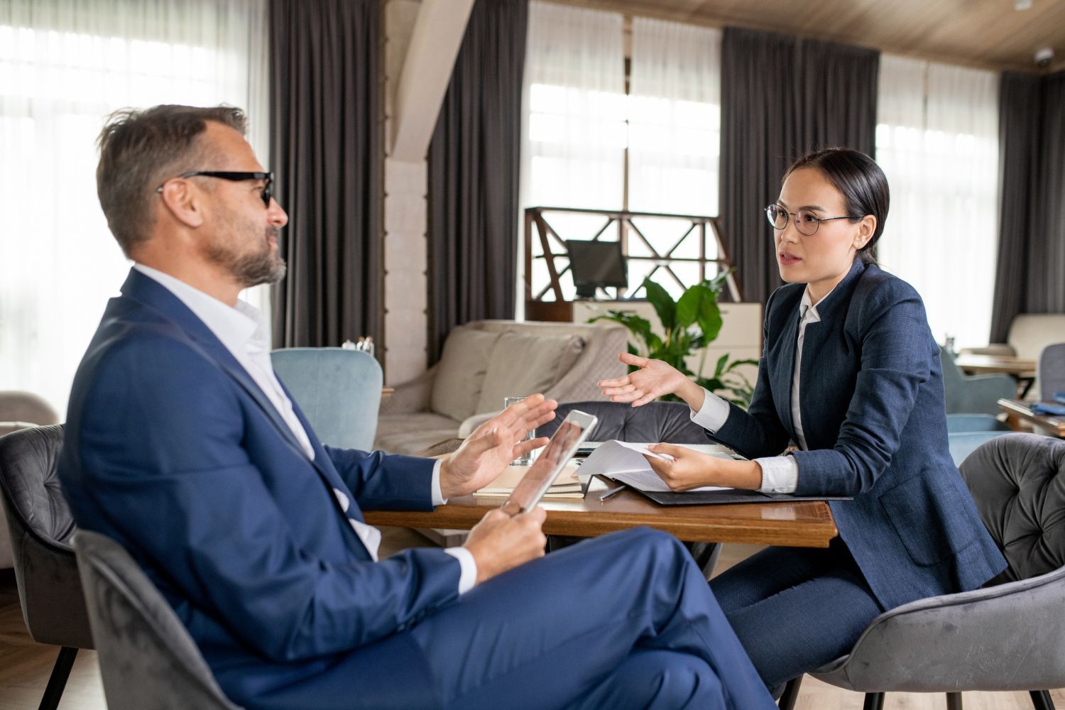 Man and woman in business attire discussing documents at a table. Indoor setting.