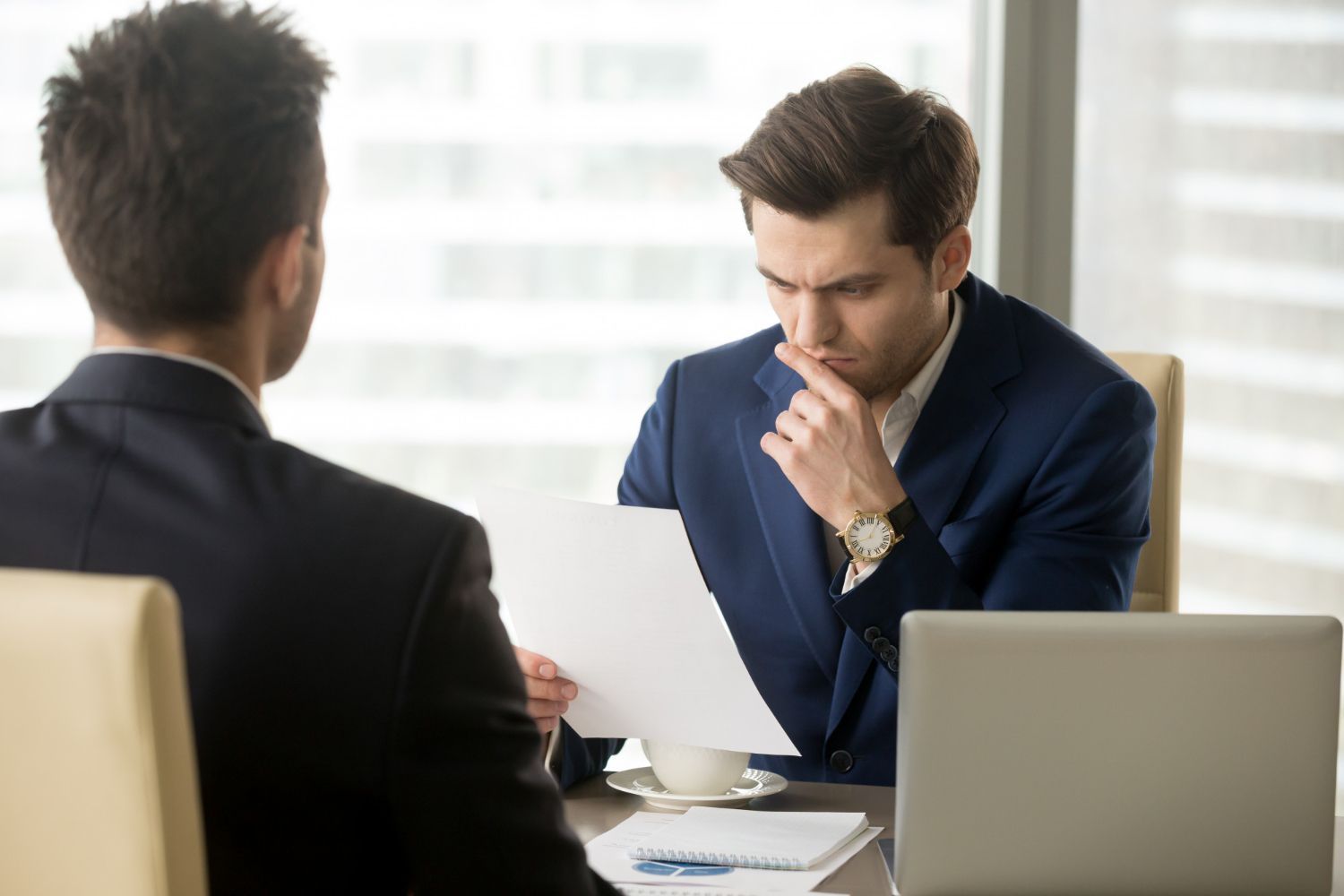 Two business professionals in suits reviewing documents, discussing strategy.