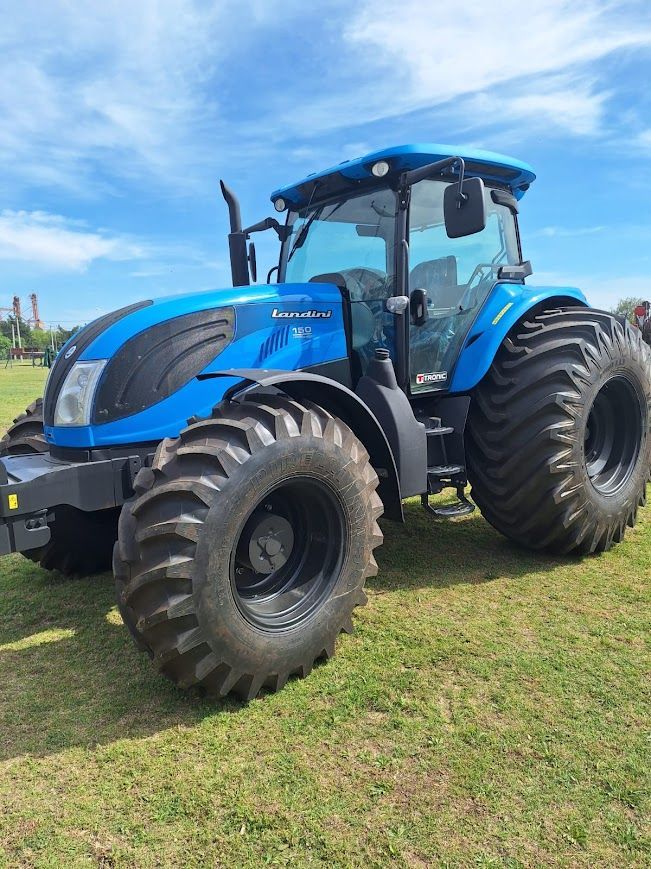 Tractor azul con neumáticos grandes en un campo de hierba bajo un cielo azul.
