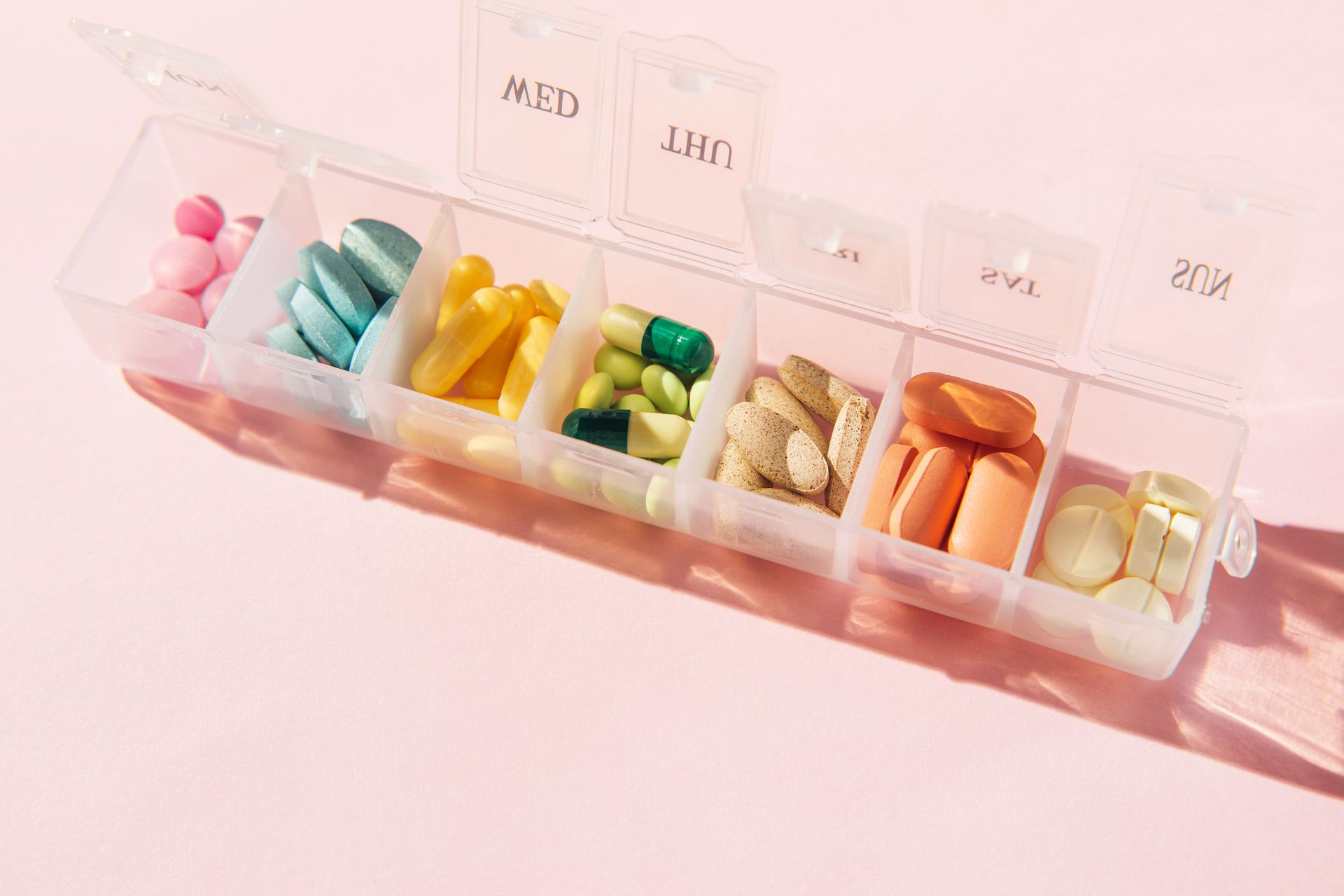 A pill box filled with different types of pills on a pink background.