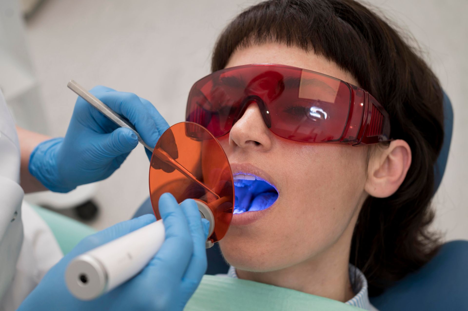 Dentista iluminando los dientes de un paciente con luz azul. El paciente lleva gafas protectoras.