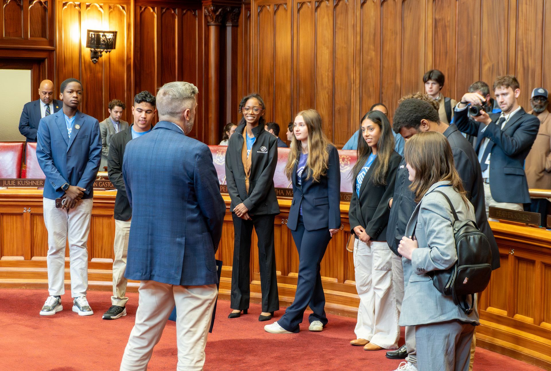A group of people are standing in a room in front of a wooden wall.