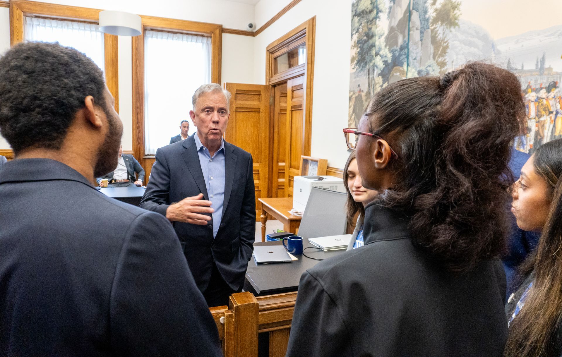 A man in a suit is talking to a group of people in a room.