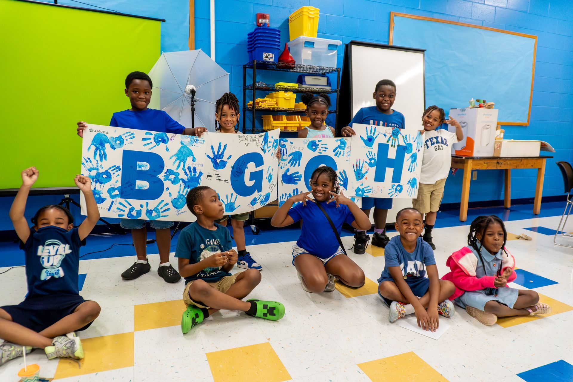 A group of children are sitting on the floor in a classroom holding a banner.