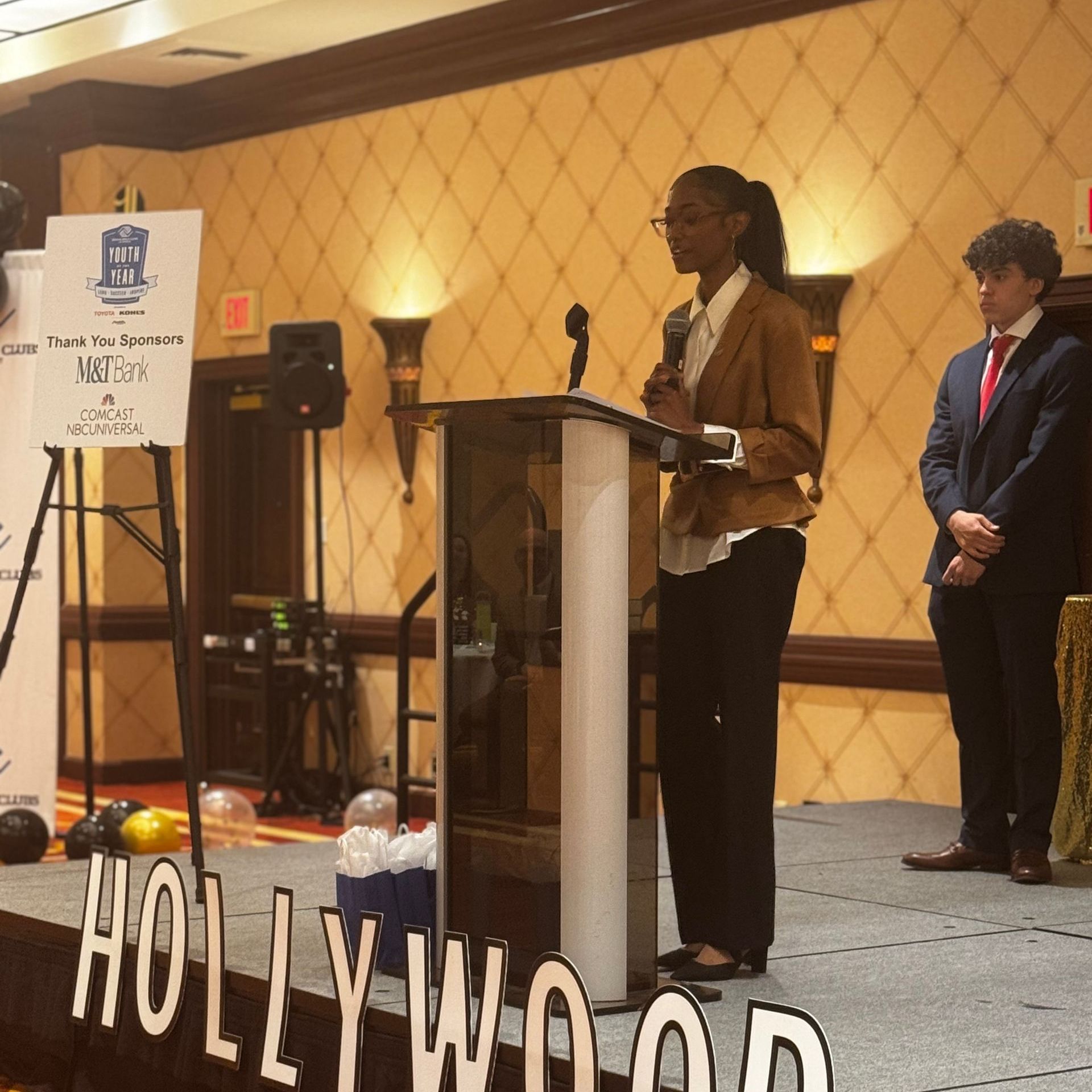 A woman stands at a podium in front of a sign that says hollywood