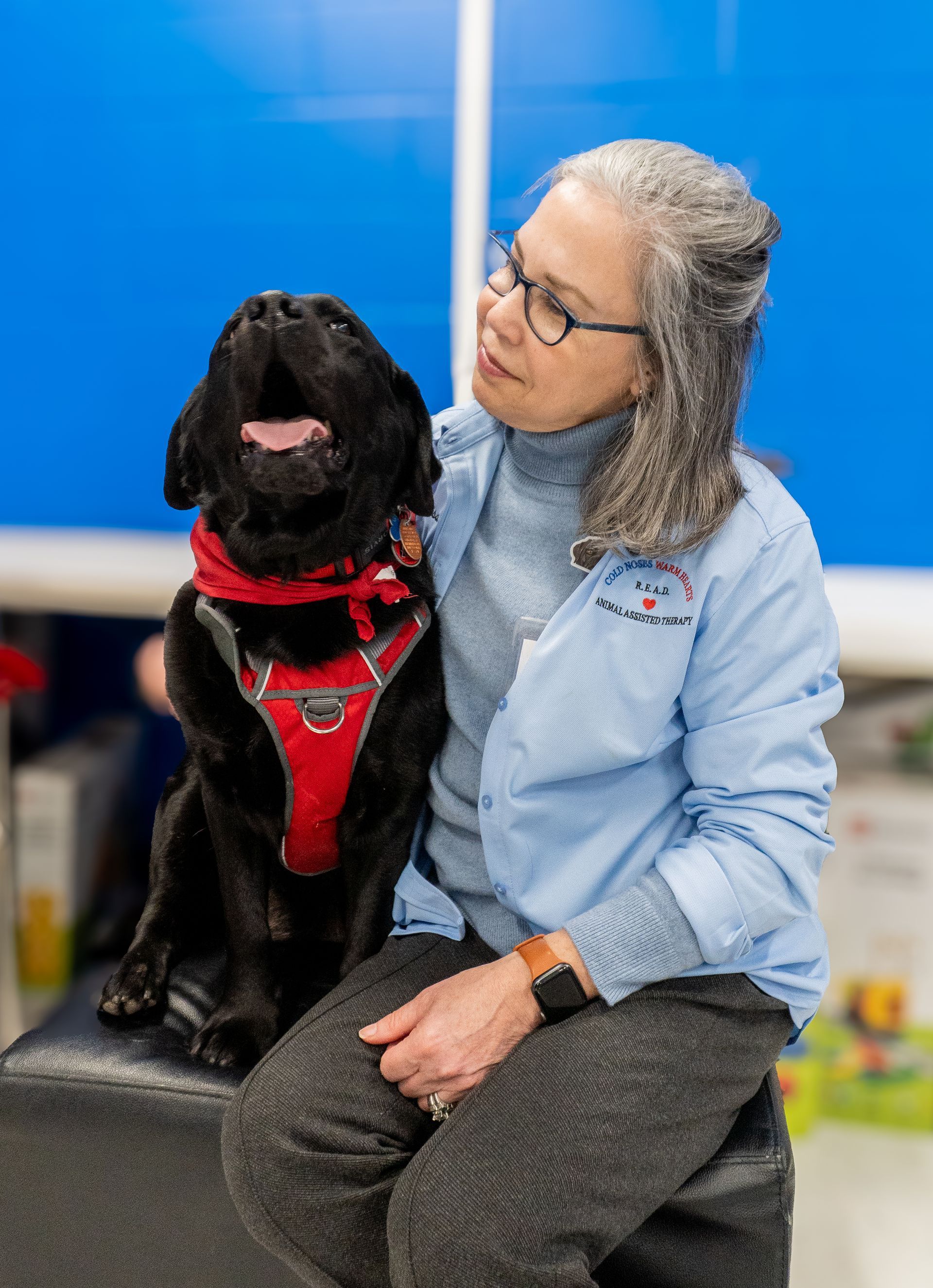 A woman is sitting on a stool next to a black dog.