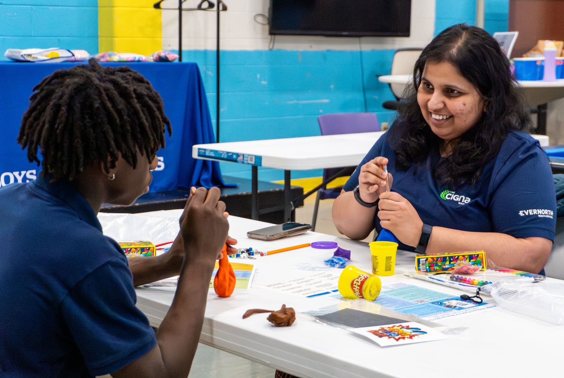 A woman and a boy are sitting at a table playing with play dough.