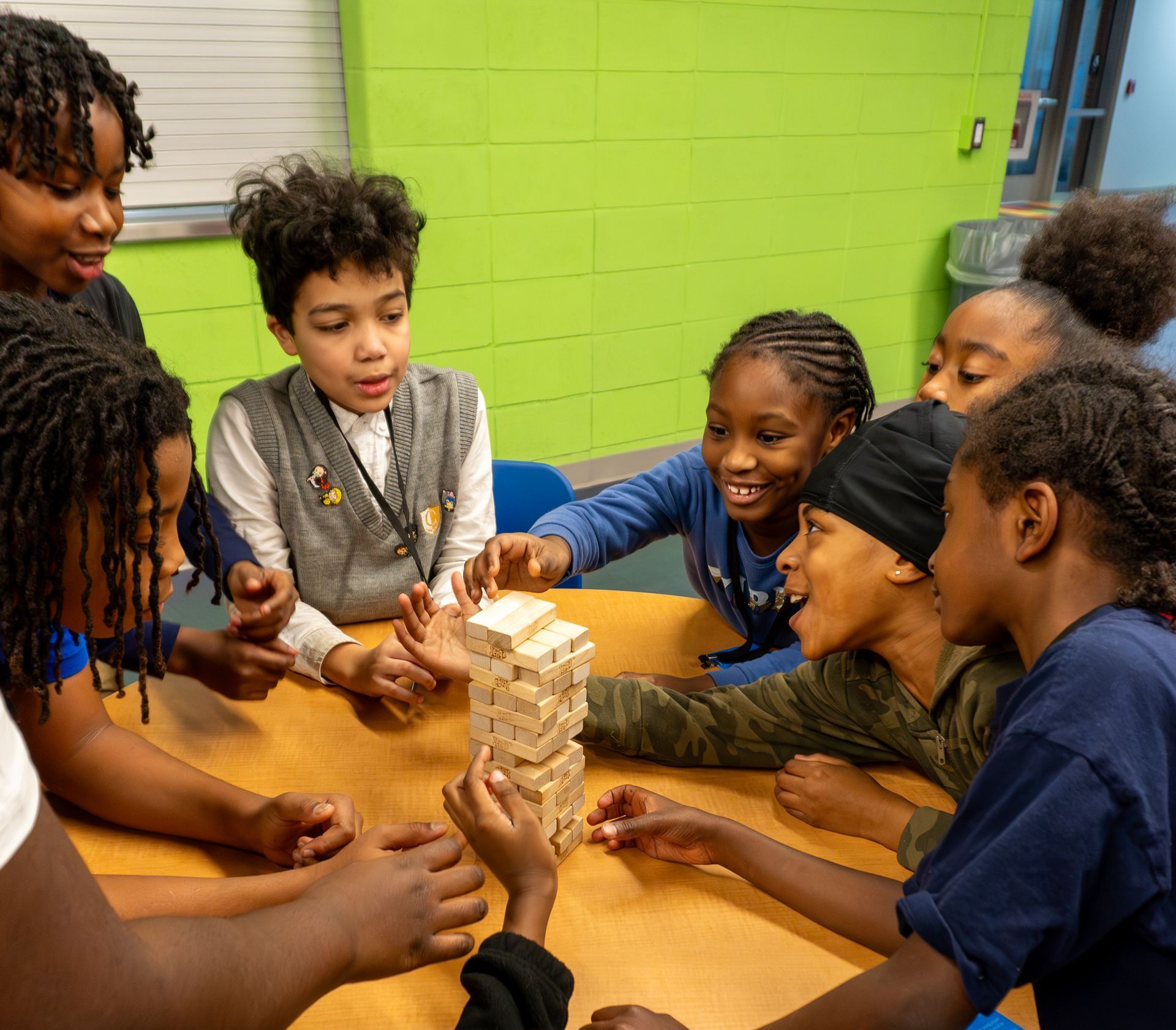 A group of children are sitting around a table playing jenga.