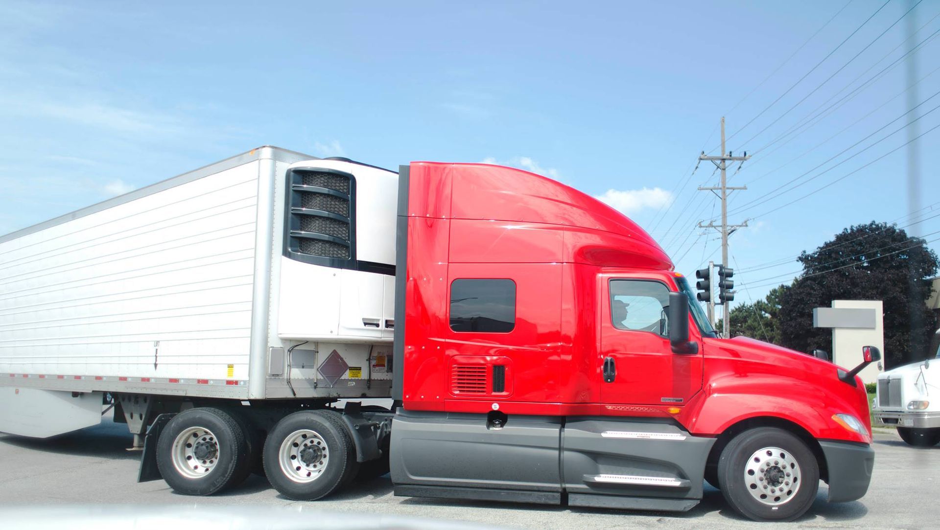 A red semi truck with a white trailer is parked on the side of the road.