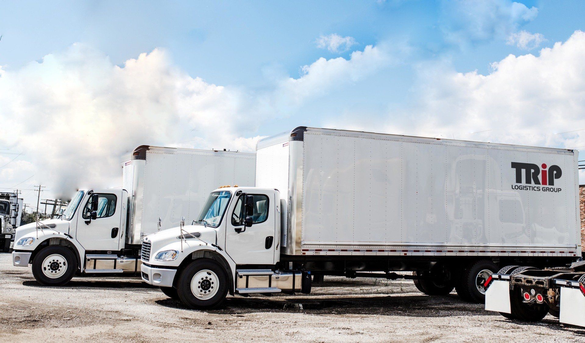 Two white semi trucks are parked next to each other in a dirt lot.