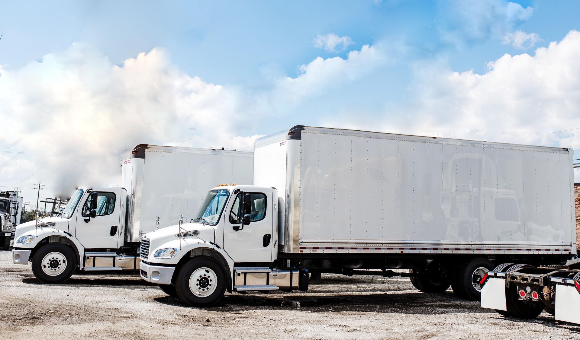 Two white semi trucks are parked next to each other in a dirt lot.