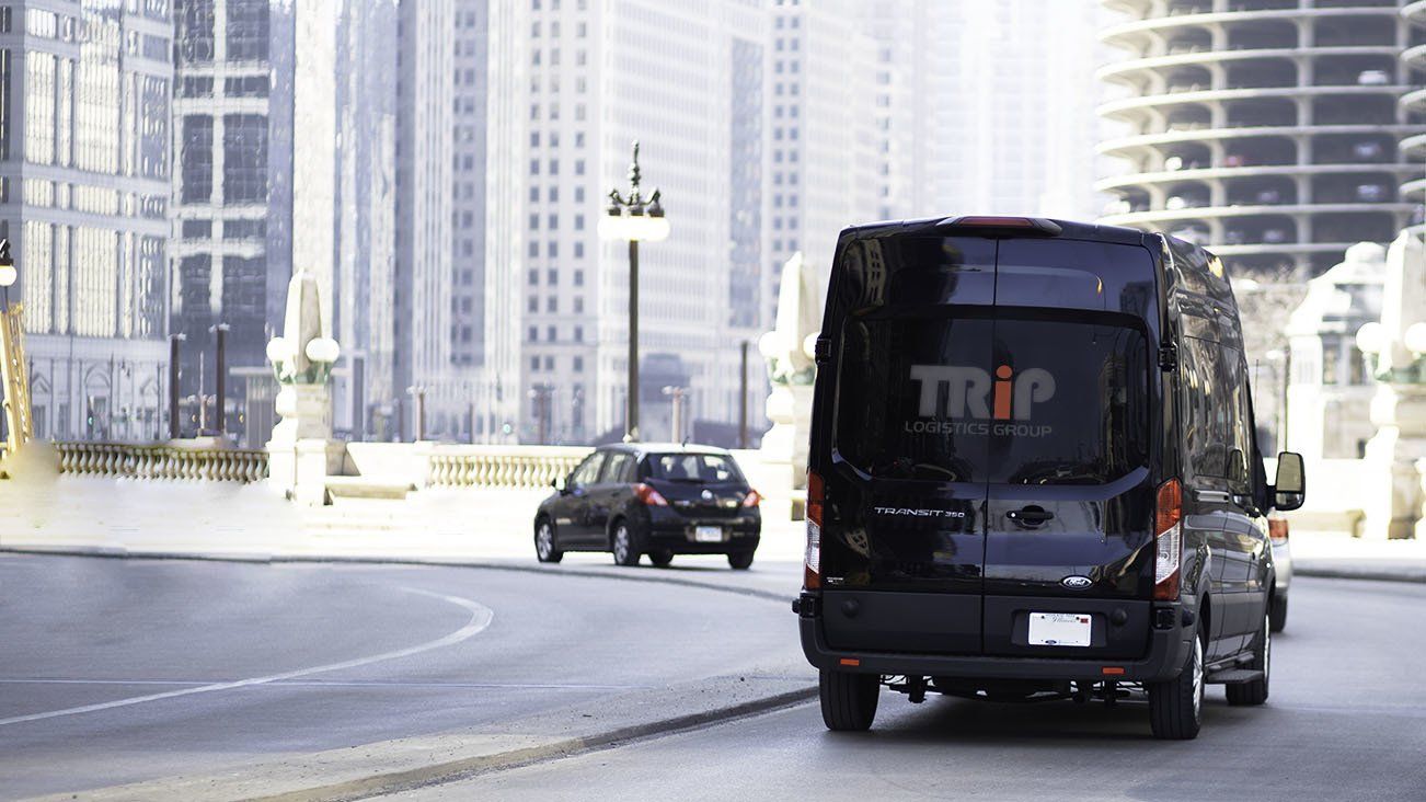 A black van with the word trip on the back is driving down a city street.