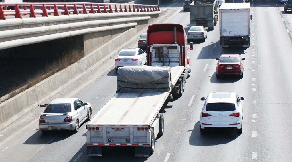 A truck with a flat bed is driving down a highway