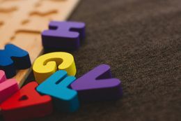 Colorful puzzle pieces in the form of capital letters from the alphabet lay scattered beside an unfinished puzzle. 