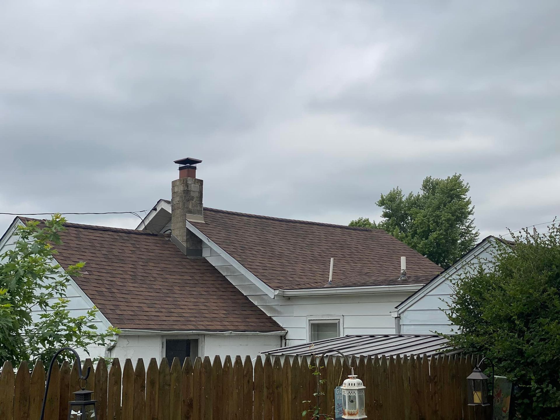 A house with a chimney on the roof is behind a wooden fence.