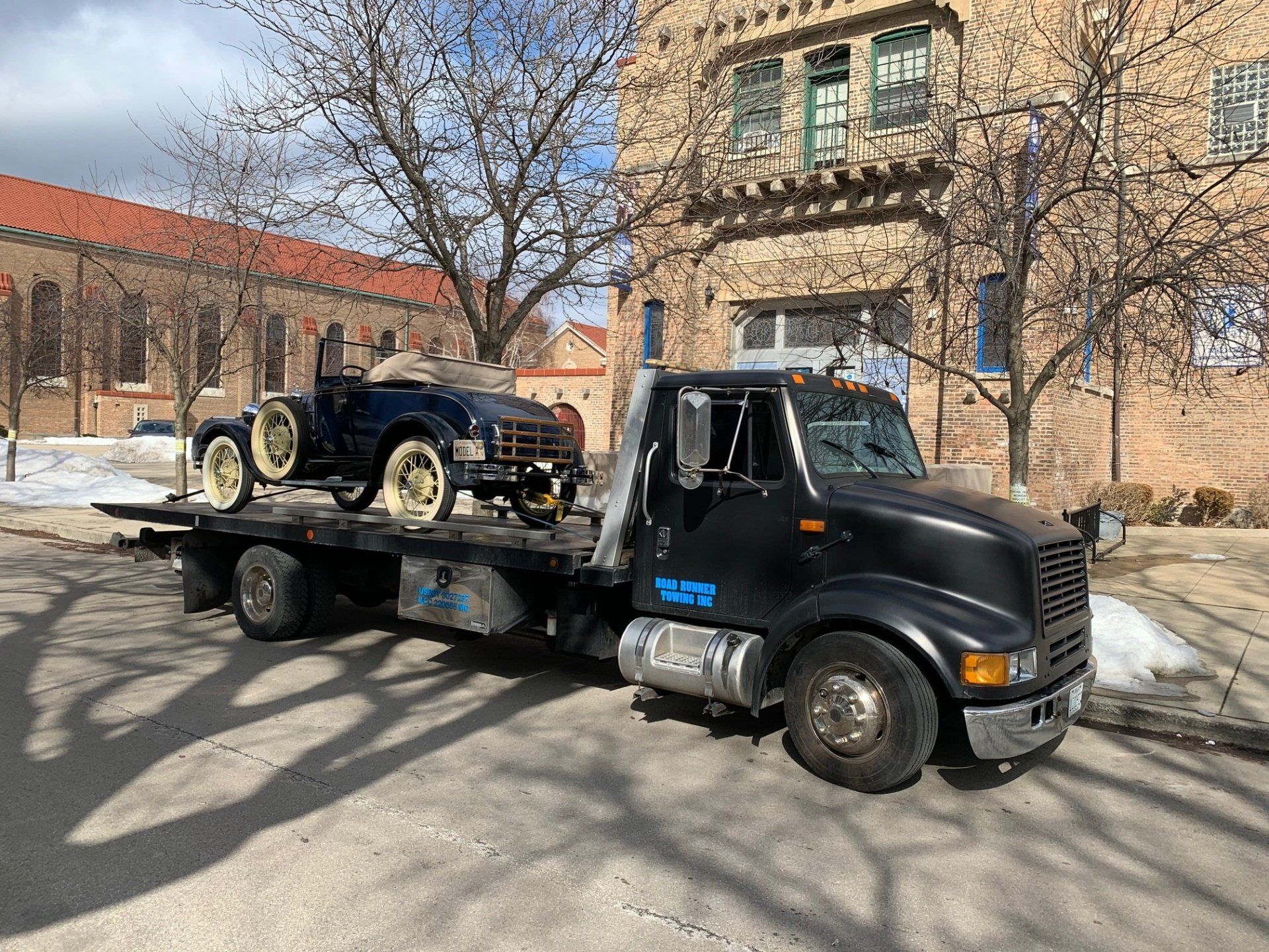 A tow truck is carrying an old car on the back of it.