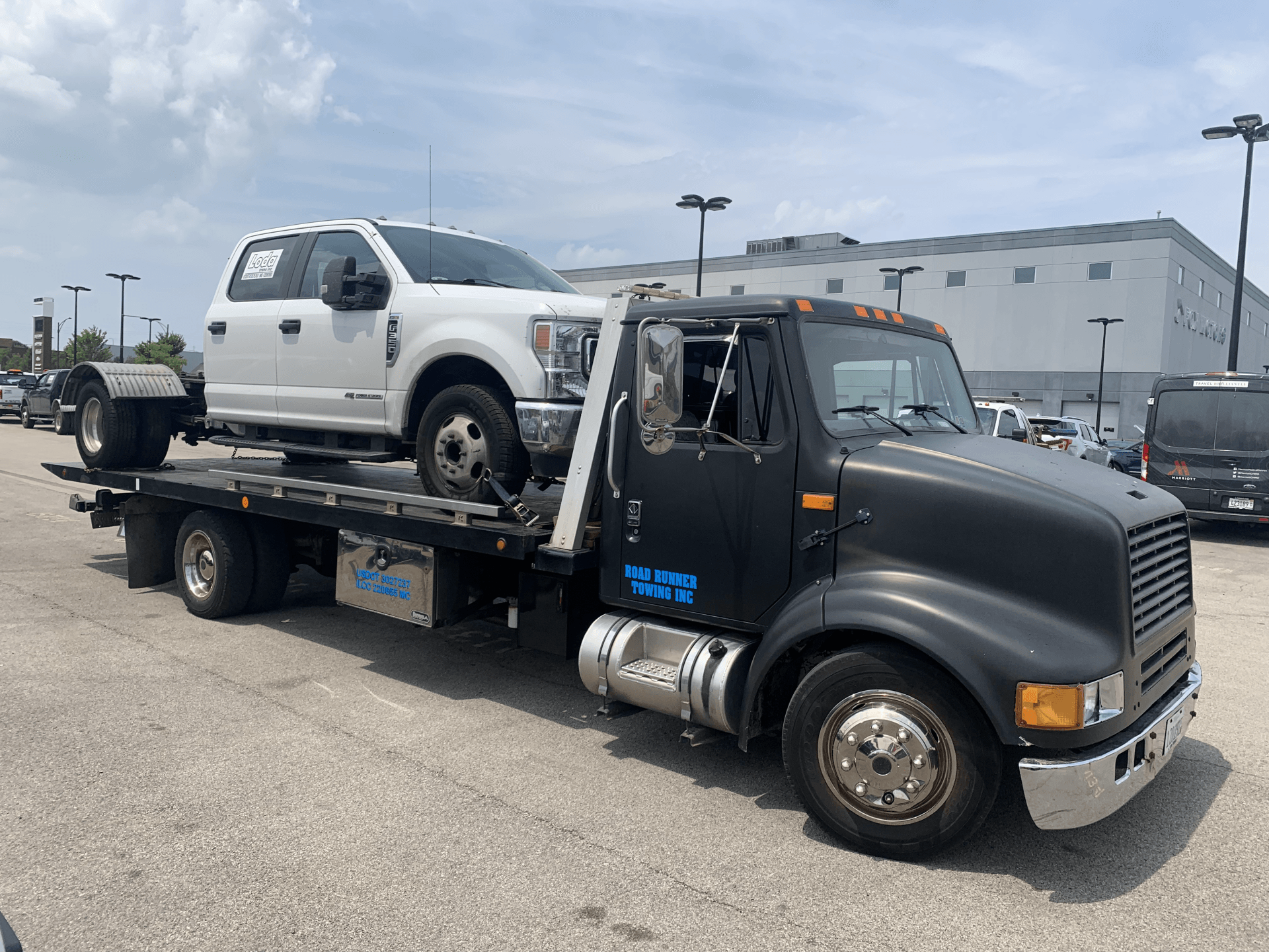 A tow truck is towing a white truck in a parking lot.