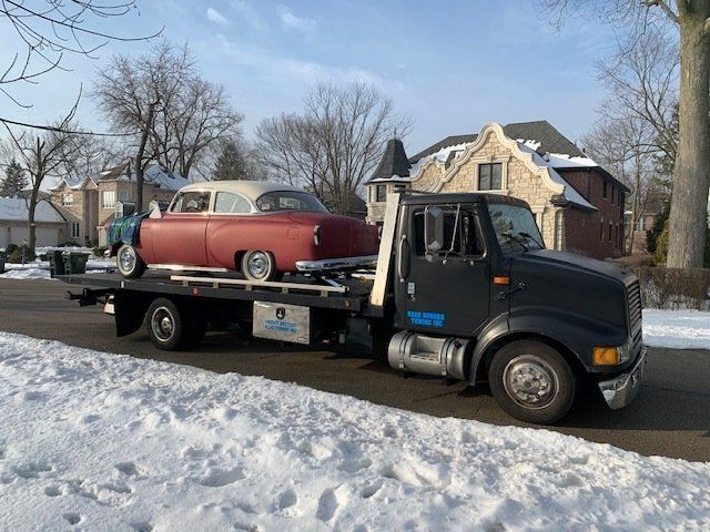 A tow truck is carrying a red car down a snowy street.