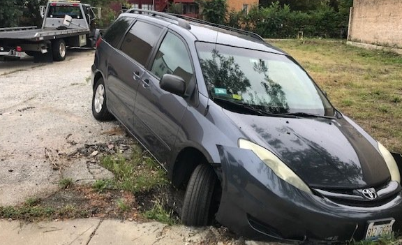 A gray minivan is parked on the side of the road next to a tow truck.