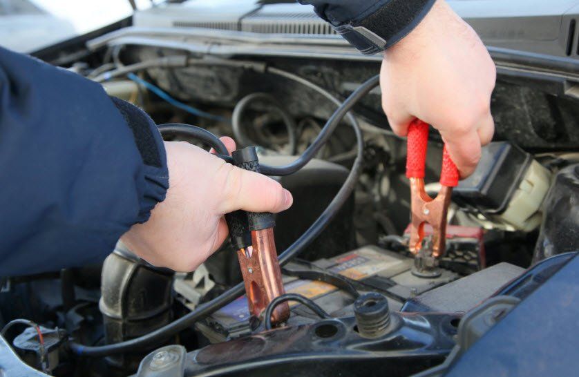 A person is charging a car battery with jumper cables.