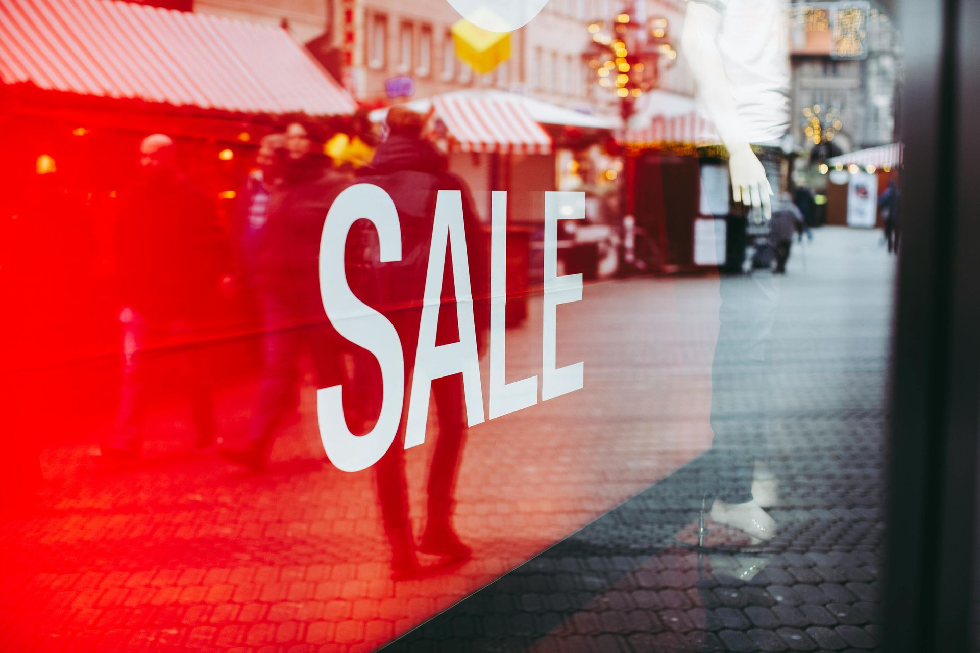 A man is standing in front of a store window with a sale sign on it.