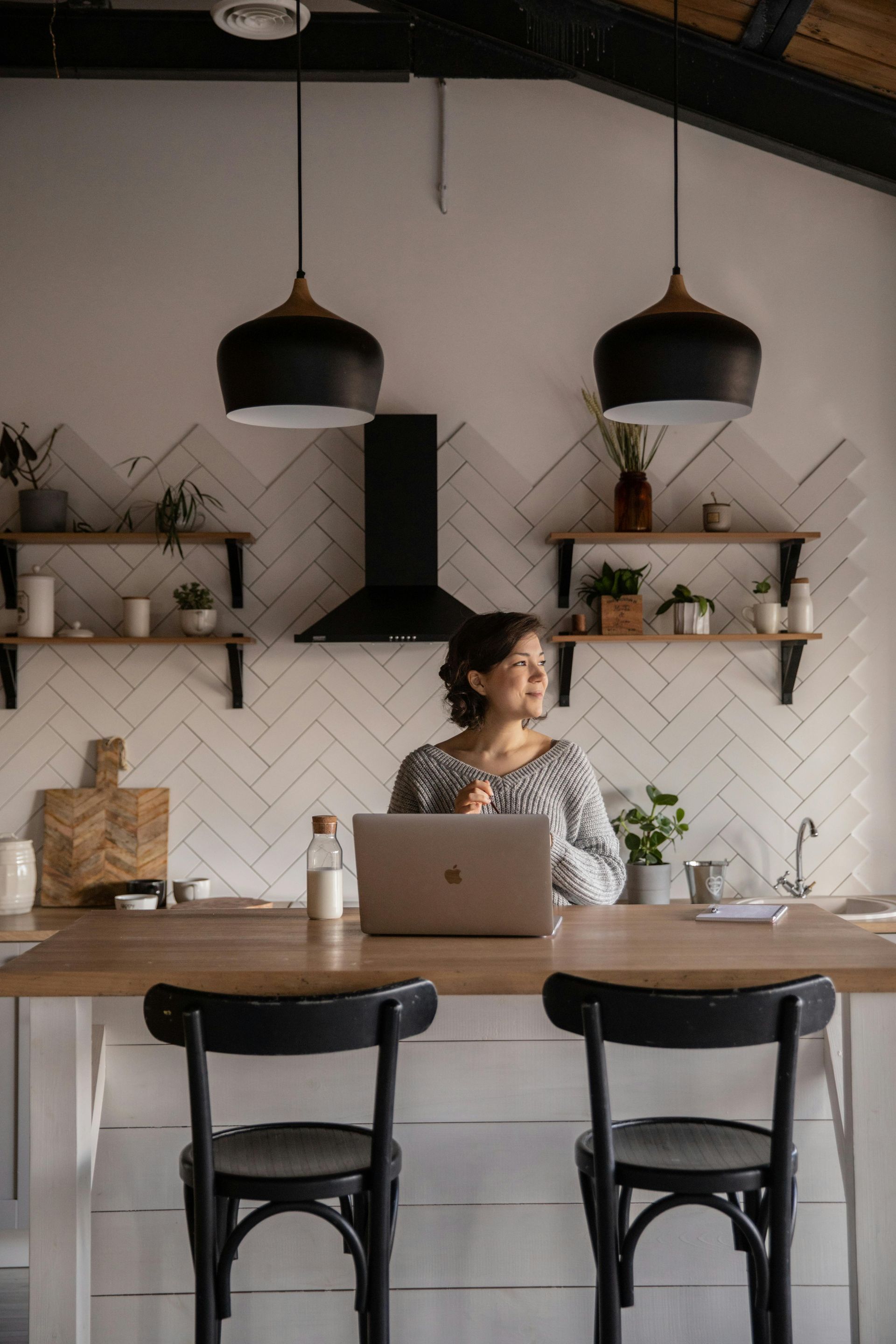 A woman is sitting at a table in a kitchen using a laptop computer.