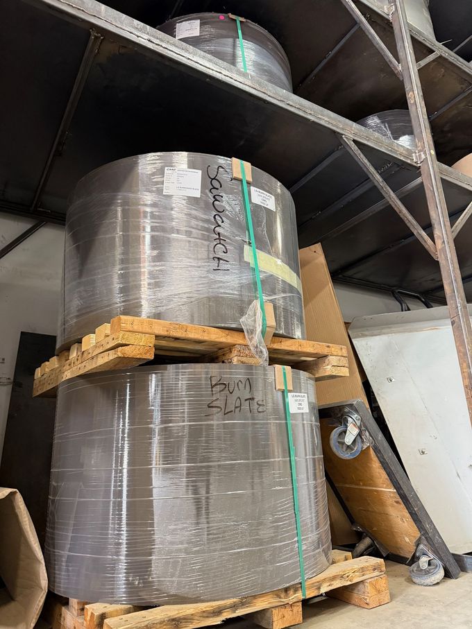Two rolls of paper are stacked on top of each other on wooden pallets in a warehouse.