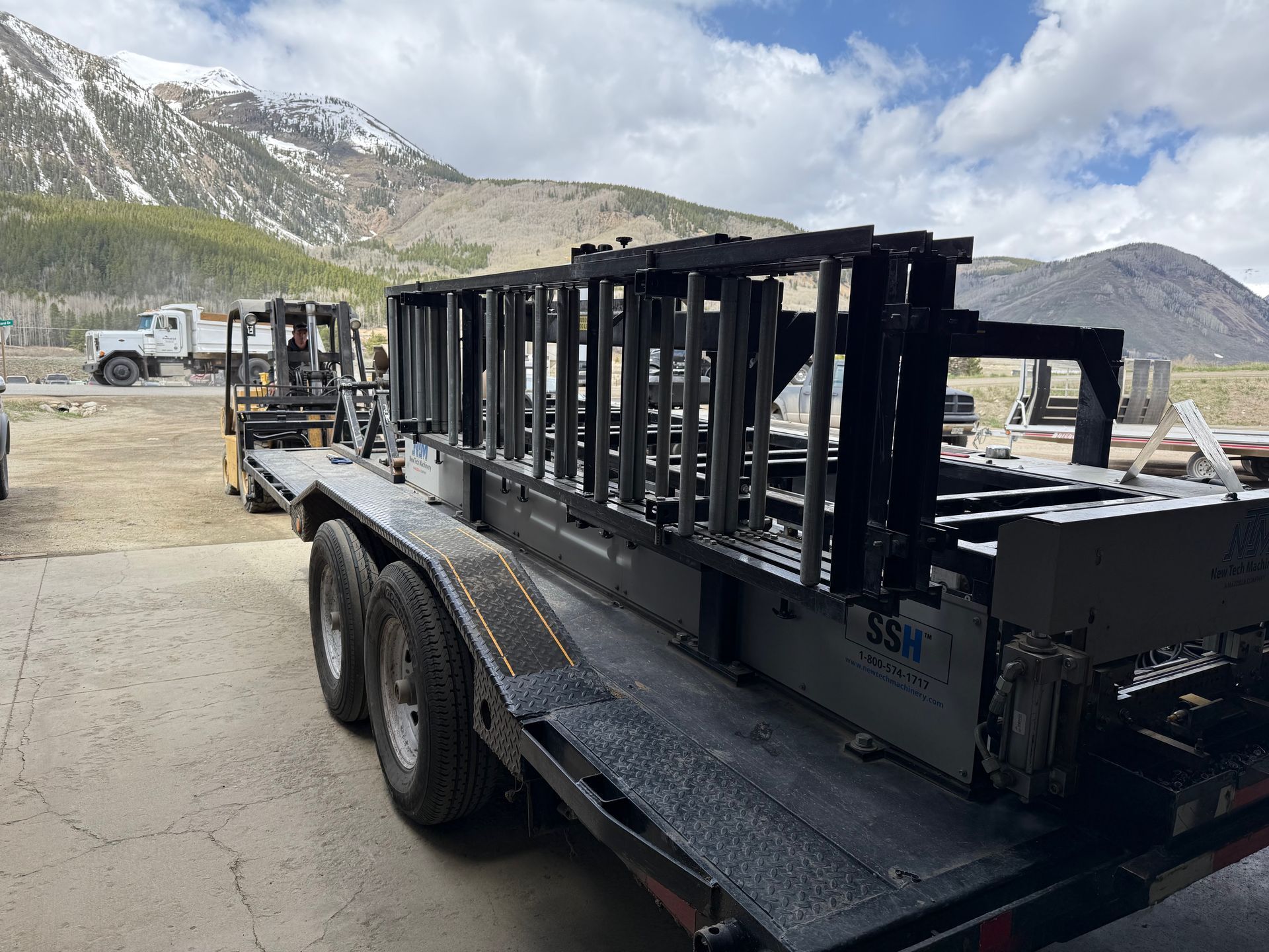 A trailer with a large metal structure on it is parked in front of a mountain.
