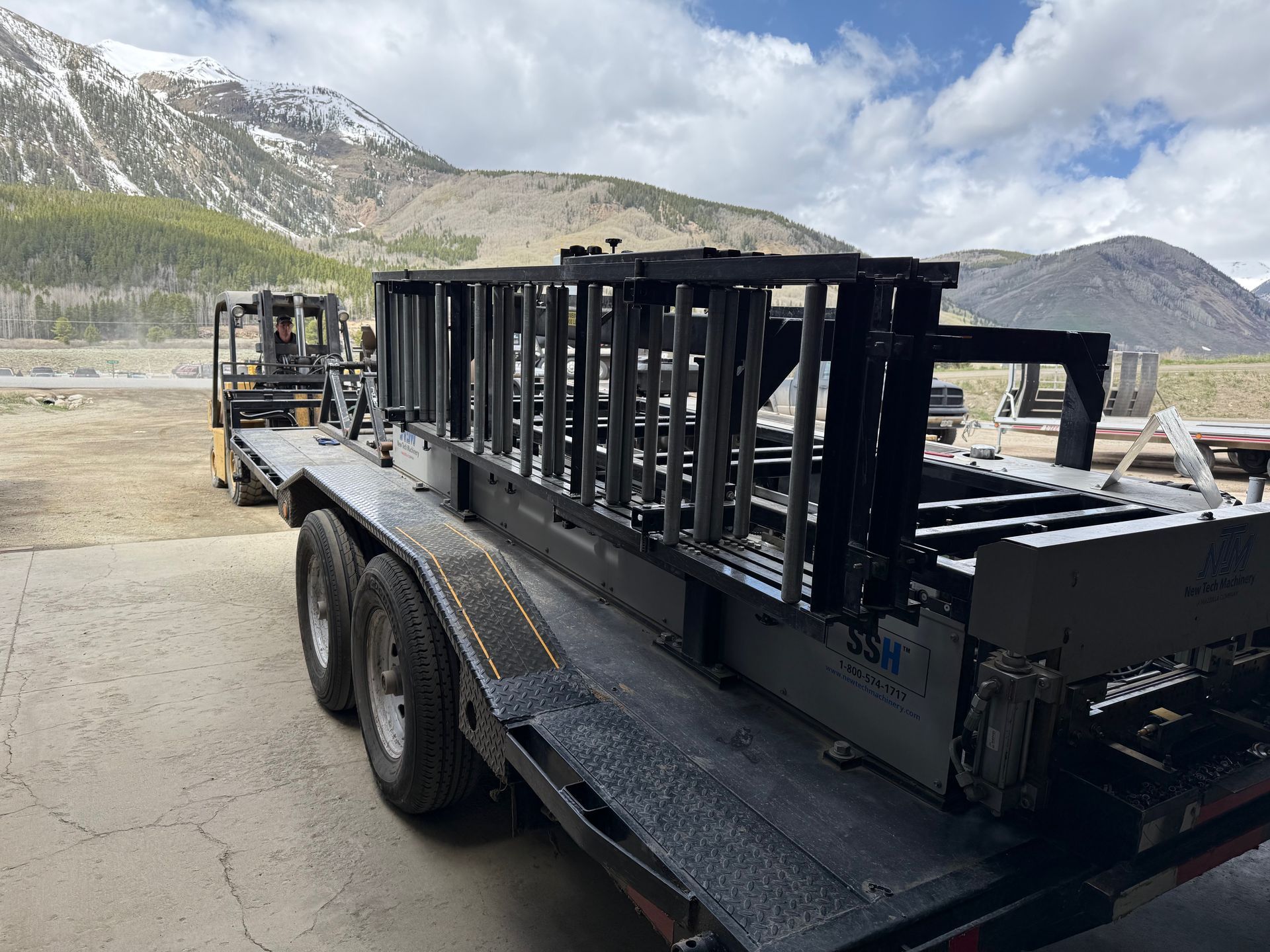 A trailer with a ladder on it is parked in front of a mountain.