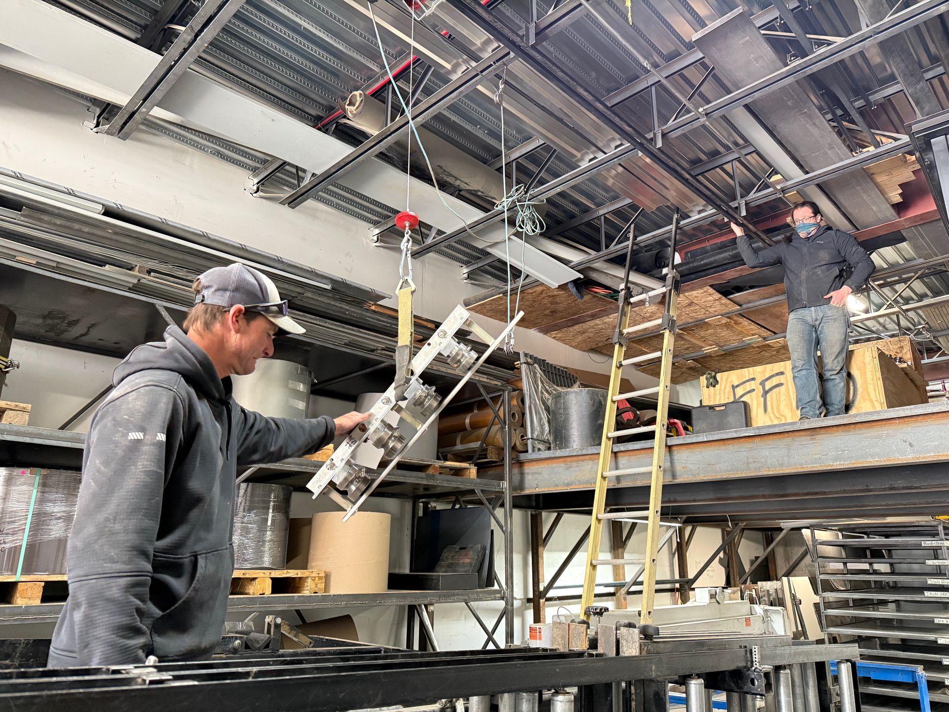 Two men are working on a metal structure in a factory.