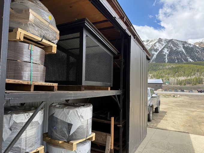 A truck is parked in front of a warehouse with mountains in the background.