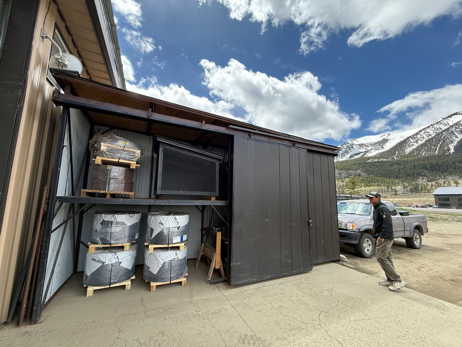 A man is standing in front of a shed with a truck parked in front of it.