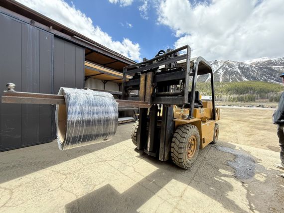 A forklift is carrying a large piece of metal in front of a building.