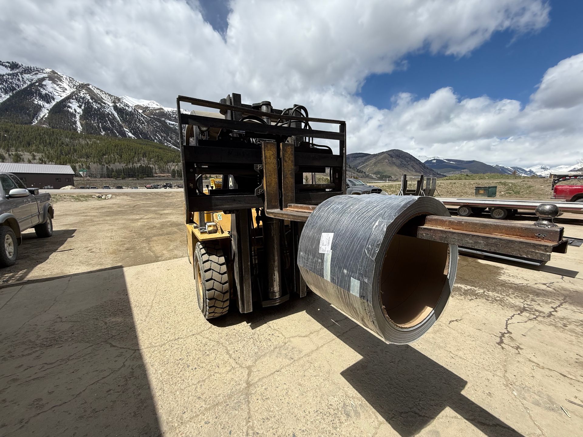 A forklift is carrying a large roll of metal