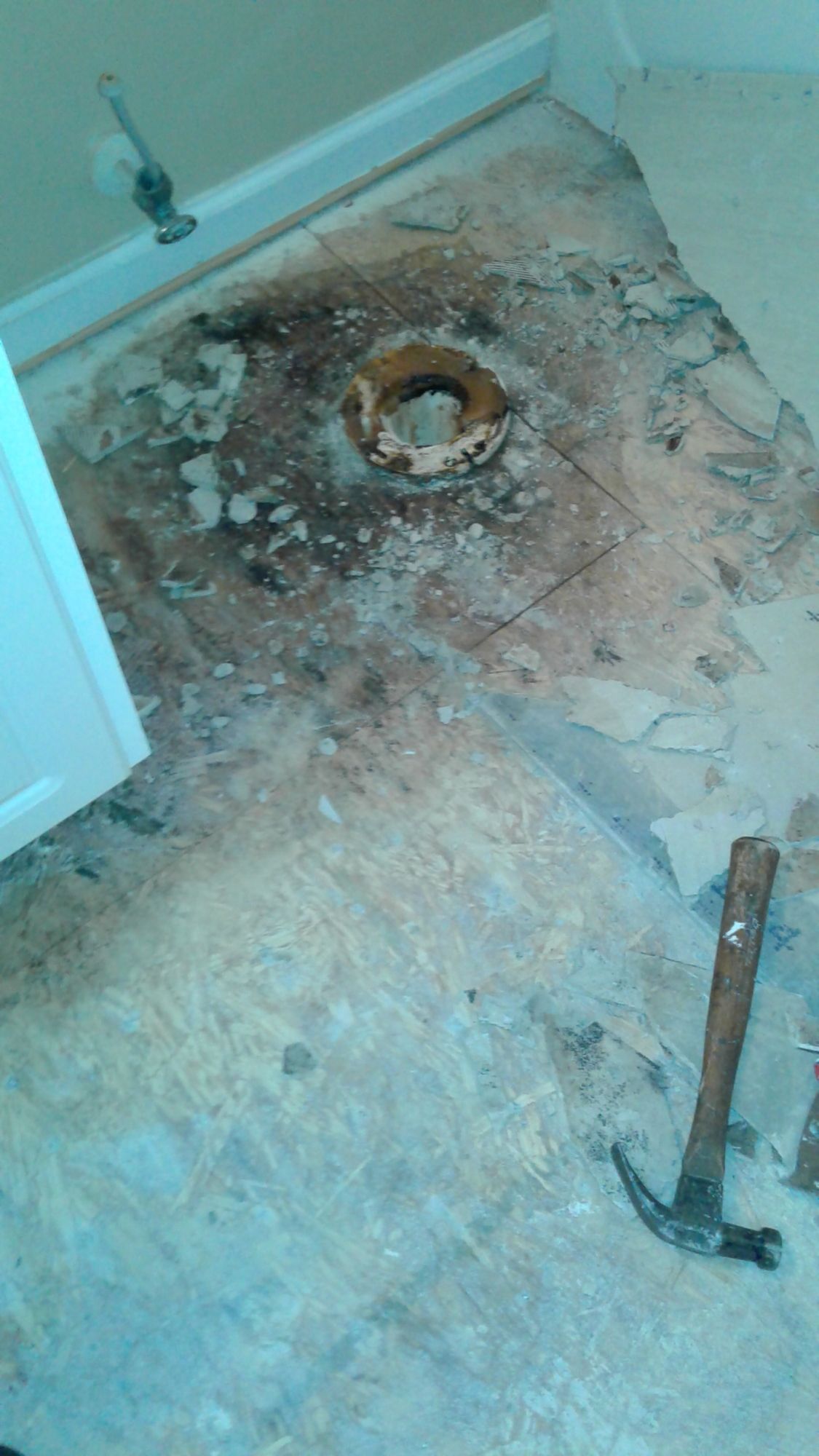 A toilet flange is being removed from the floor of a bathroom.