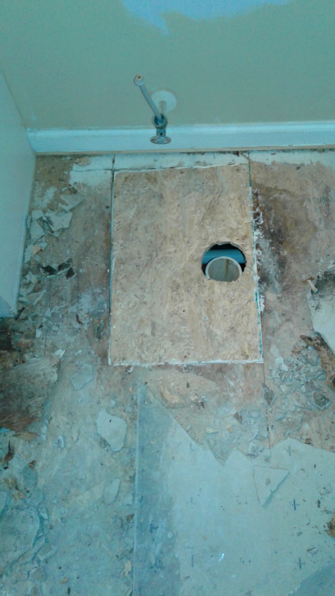 A piece of plywood is sitting on the floor next to a hole in the wall.