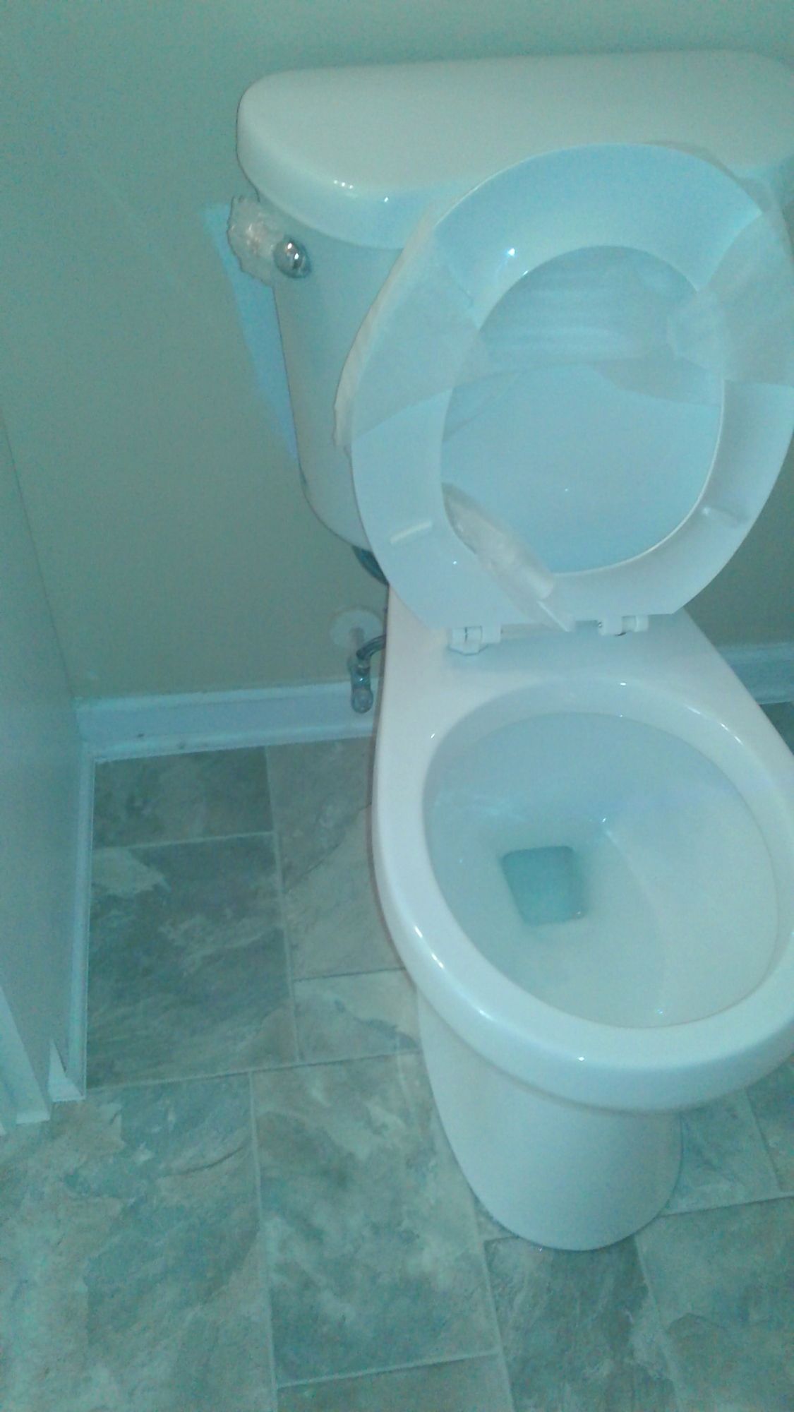 A white toilet is sitting on a tiled floor in a bathroom.