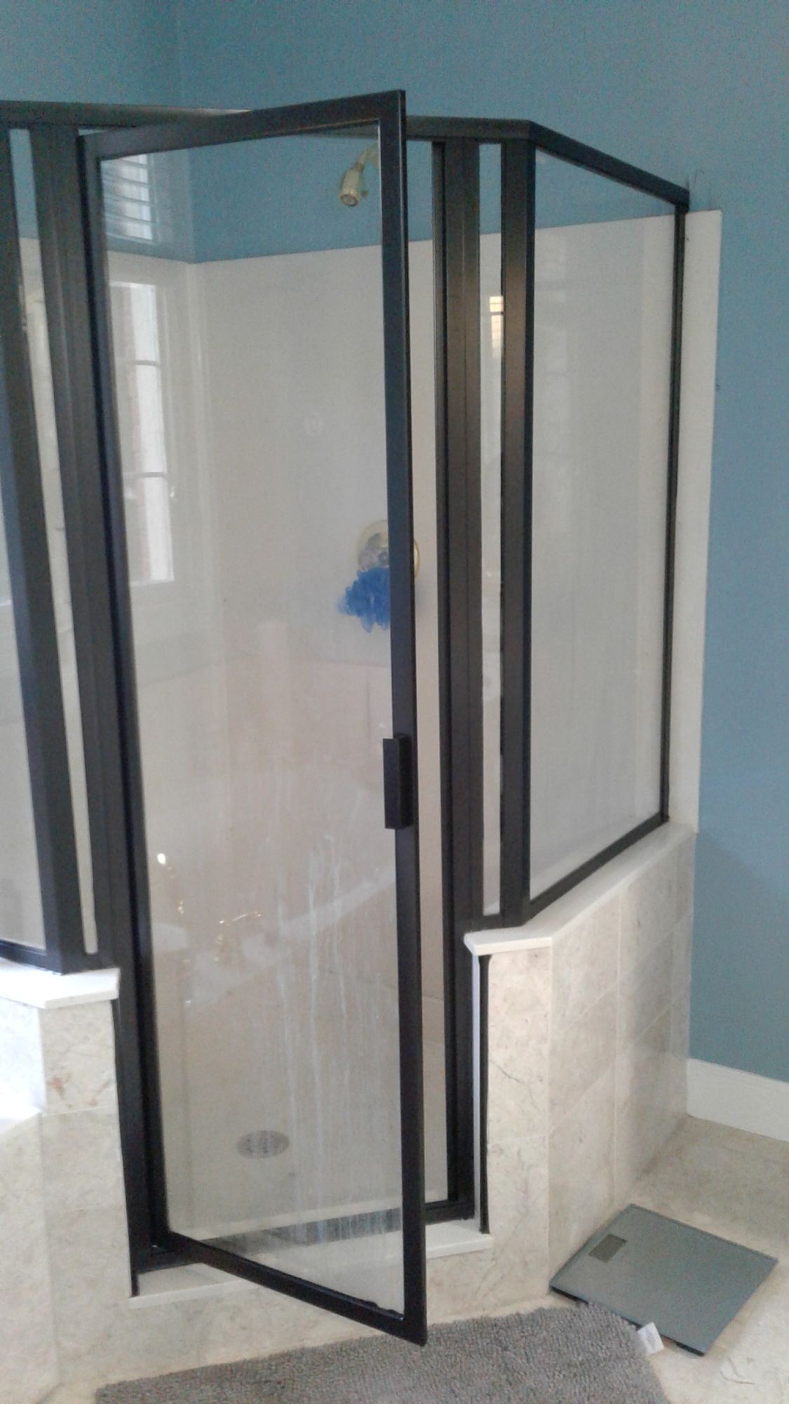 A bathroom with a shower stall and a scale on the floor.