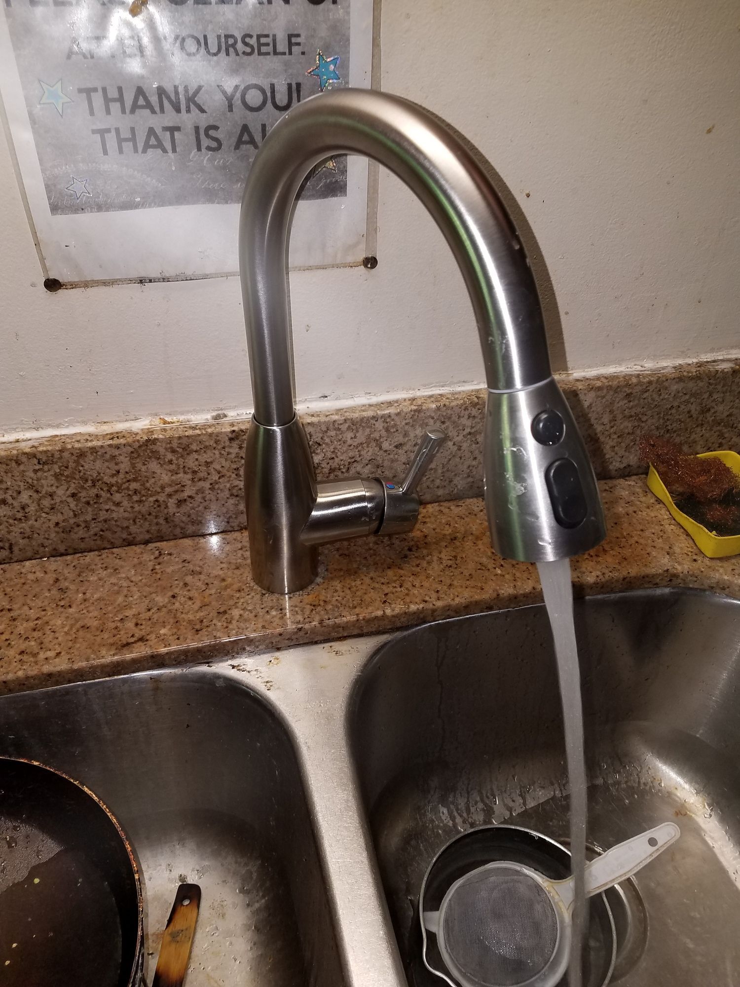 A stainless steel faucet is running water into a kitchen sink.